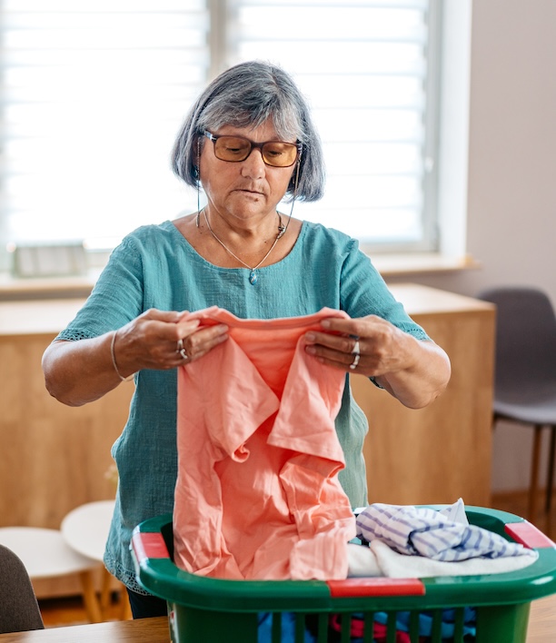Older woman folding laundry at home, representing someone who has managed her household for decades now weighing whether to handle this task differently