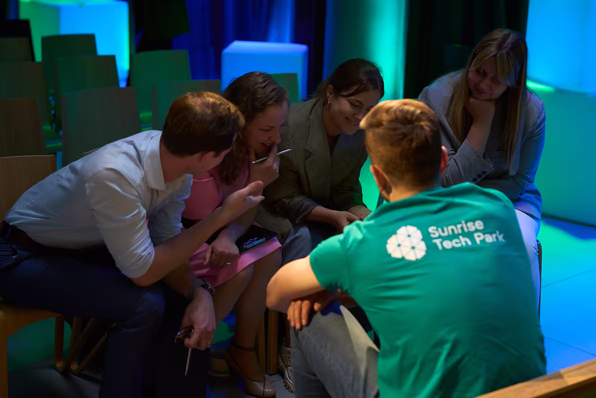 Team of smiling people are sitting in a circle and talking about something.