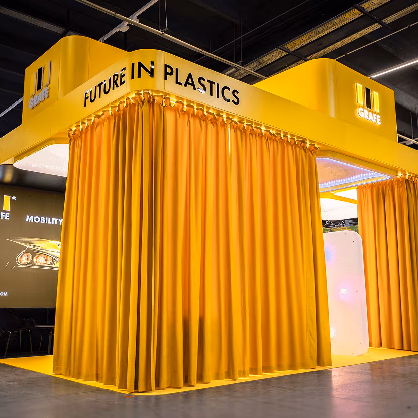 Stoisko targowe z żółtymi zasłonami, logo i napisem "Future in Plastics".