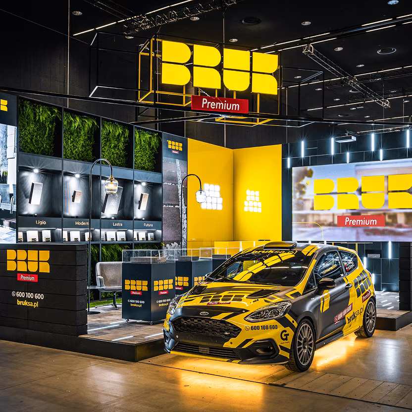 Stoisko reklamowe Bruk Premium z oświetleniem i oznakowanym samochodem.