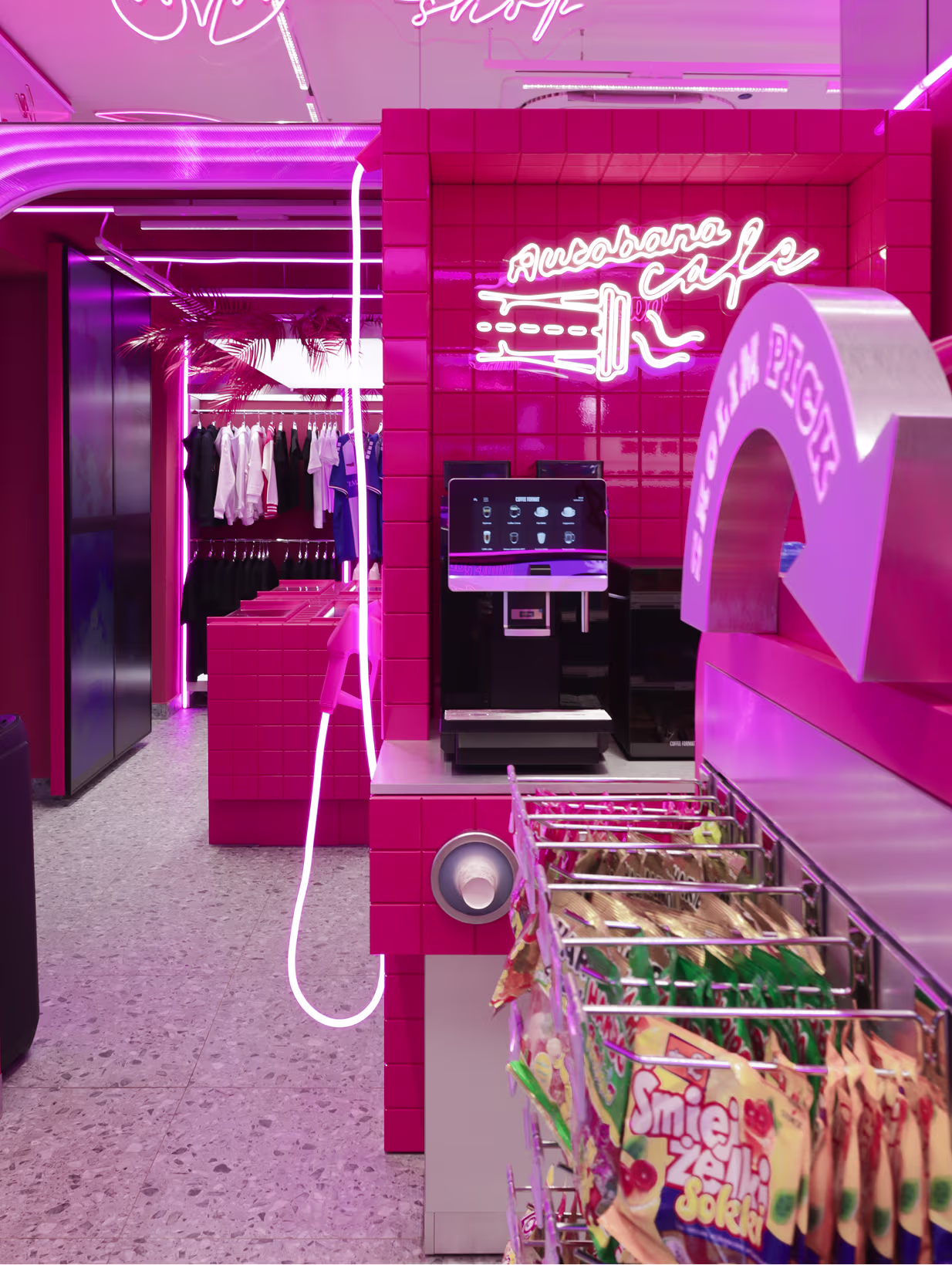 Strefa kawowa Autobana Café z automatem do kawy i neonem, w tle wieszaki ubrań Stacji Skolim
