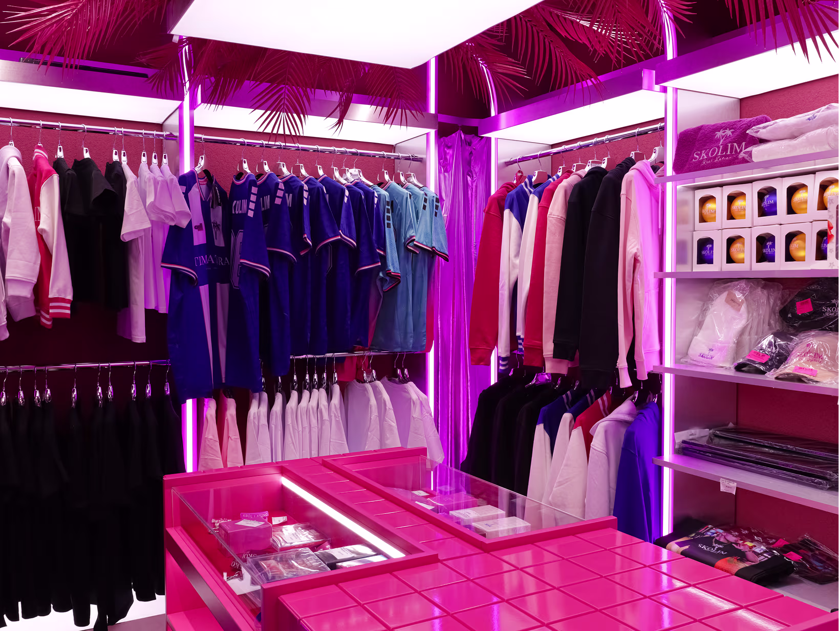 Strefa odzieżowa butiku Stacja Skolim z kolekcją bluz i koszulek, regałem Skolim i różowym neonem
