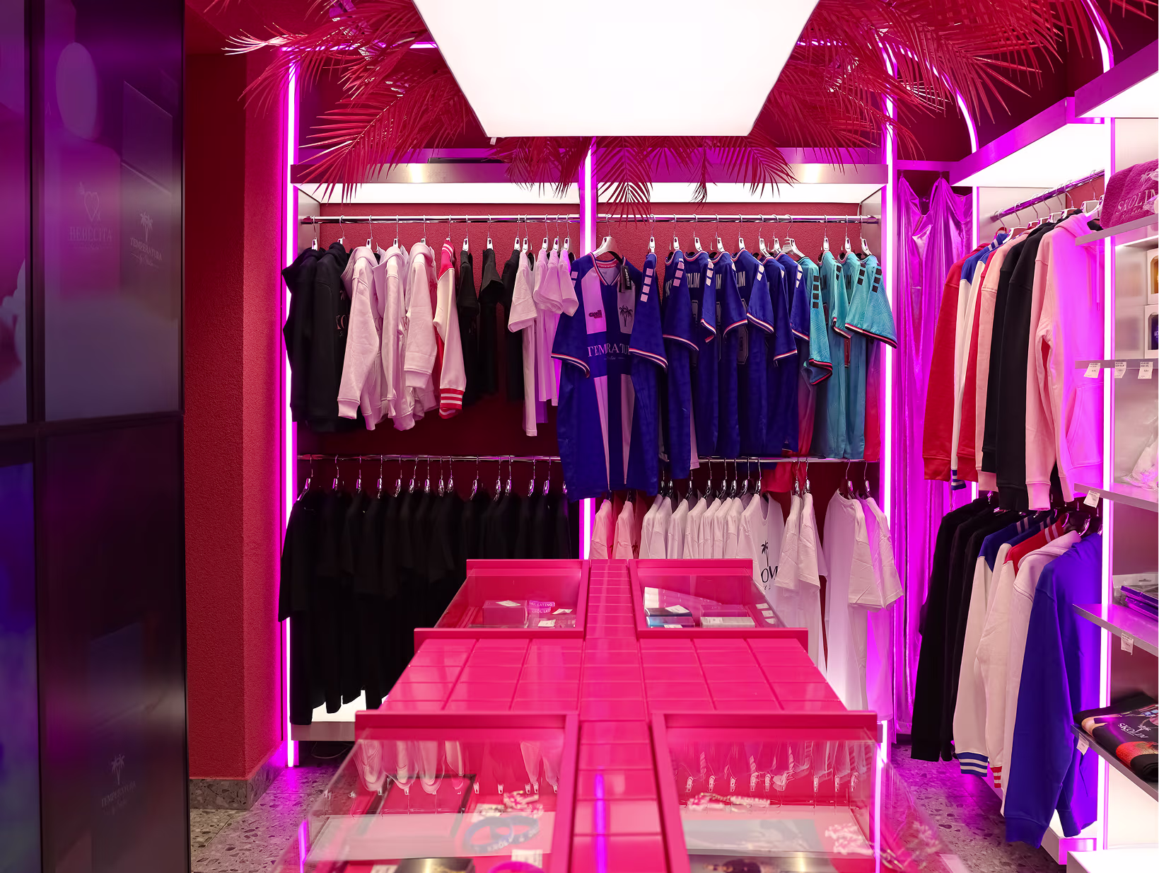 Sala sklepu Stacja Skolim z kolekcją ubrań na wieszakach, różowymi kolumnami neonowymi i palmowymi dekoracjami
