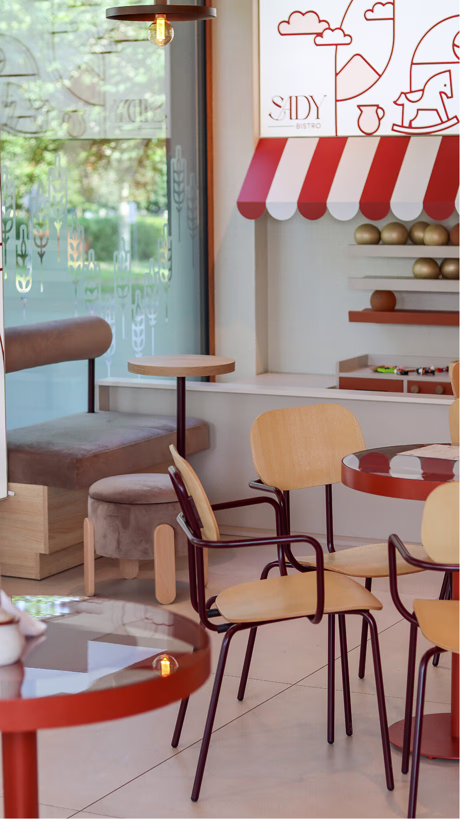 Sala Sady Bistro z drewnianymi krzesłami, czerwonymi stolikami i graficznym kącikiem dziecięcym