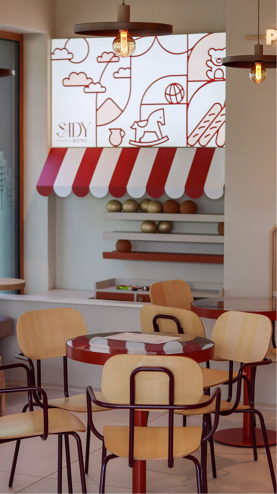 Strefa jadalna Sady Bistro z drewnianymi krzesłami, czerwonymi stolikami i graficzną ścianą dziecięcą