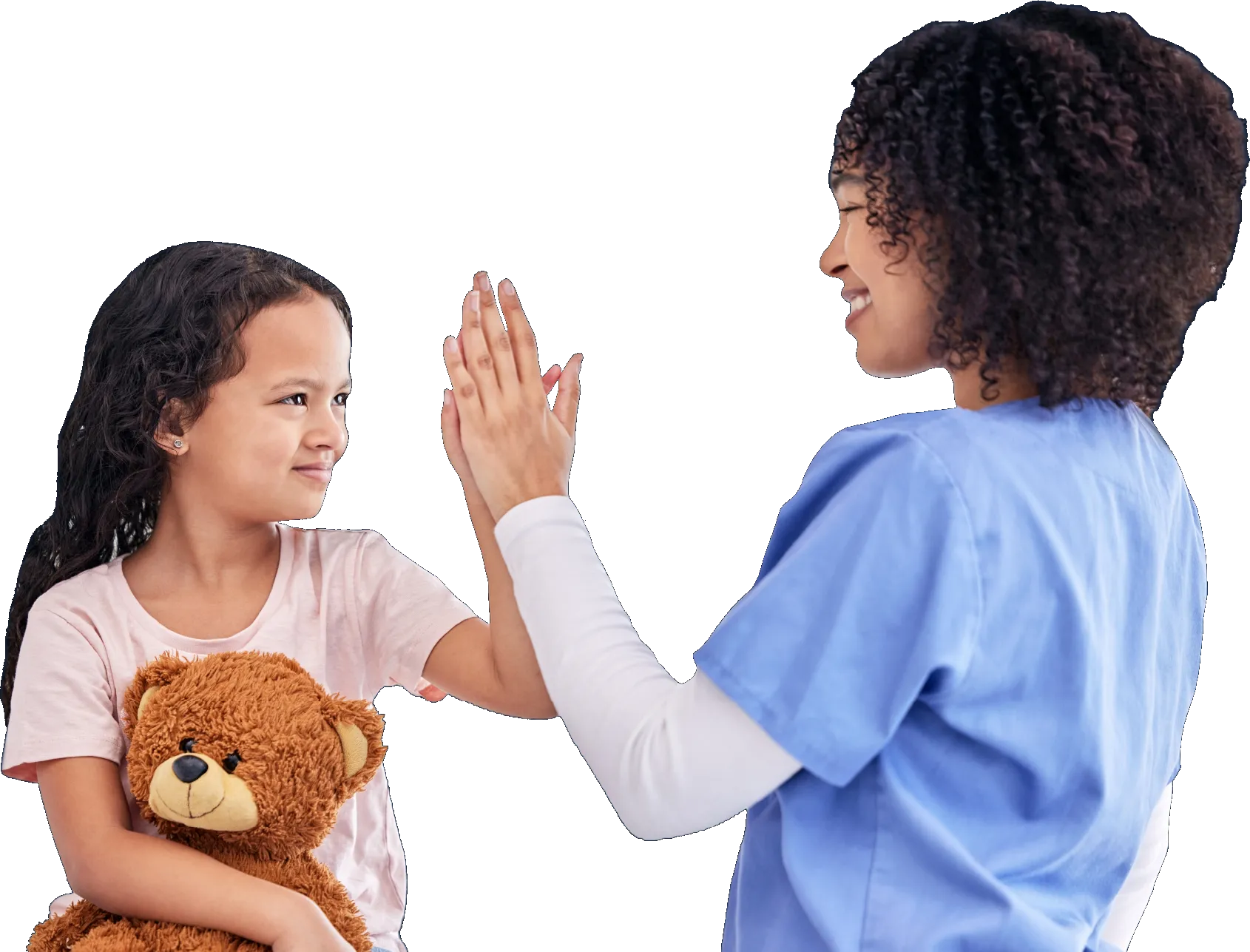 Smiling female healthcare worker in blue scrubs giving a high-five to a young girl holding a teddy bear.