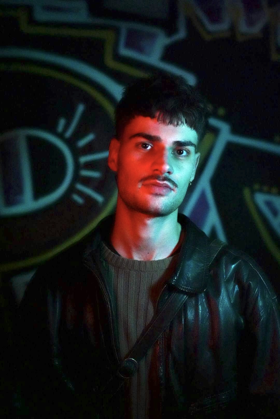 Young man wearing a leather jacket illuminated by red and blue lights with a graffiti background.