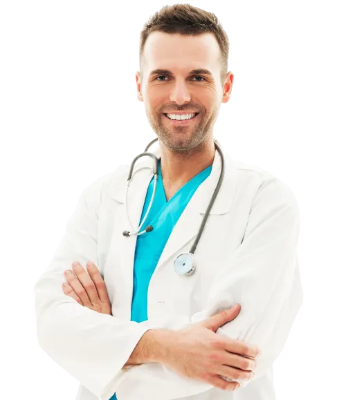 A doctor in a white coat and blue scrubs poses with his arms crossed in a hospital setting.