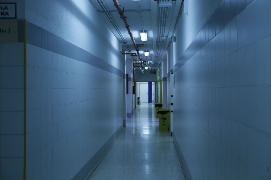 A deserted, dimly lit hallway with tiled walls and overhead lights.