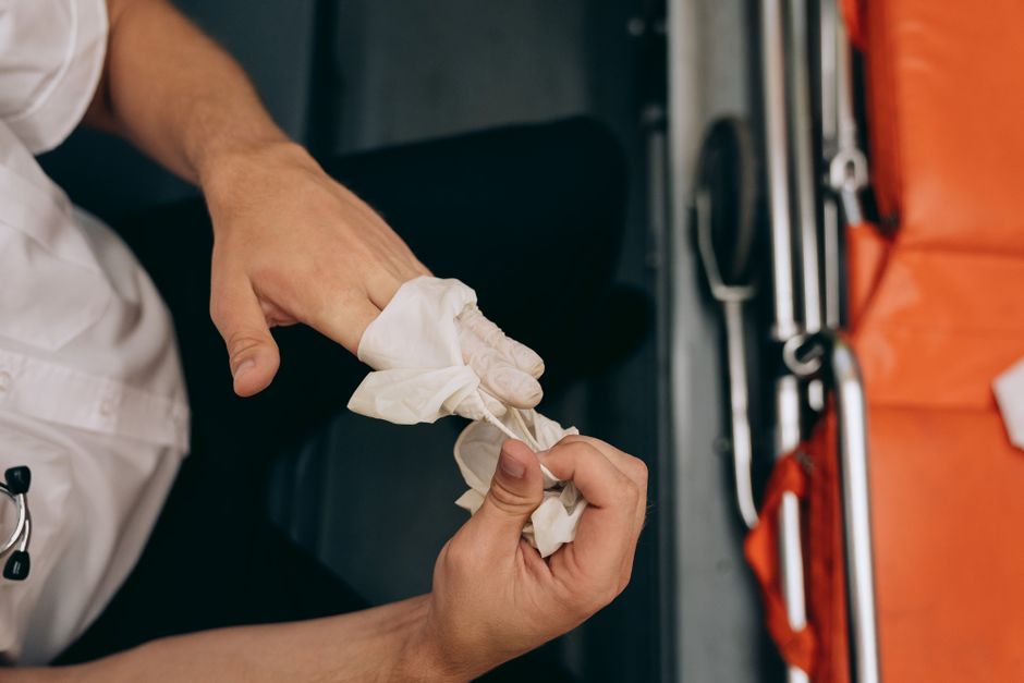 Close-up of a medical worker removing gloves in an ambulance setting, emphasizing hygiene and care.