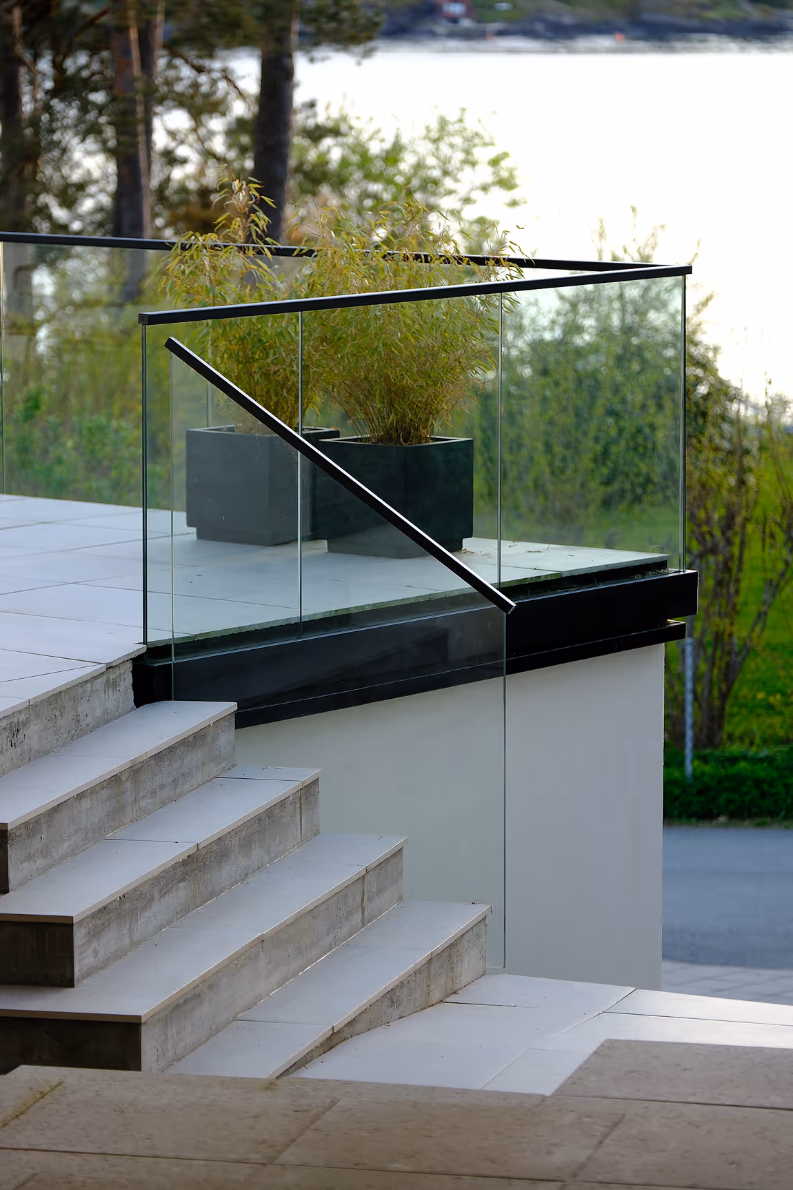 Modern outdoor staircase with glass railing and two potted plants on the landing.