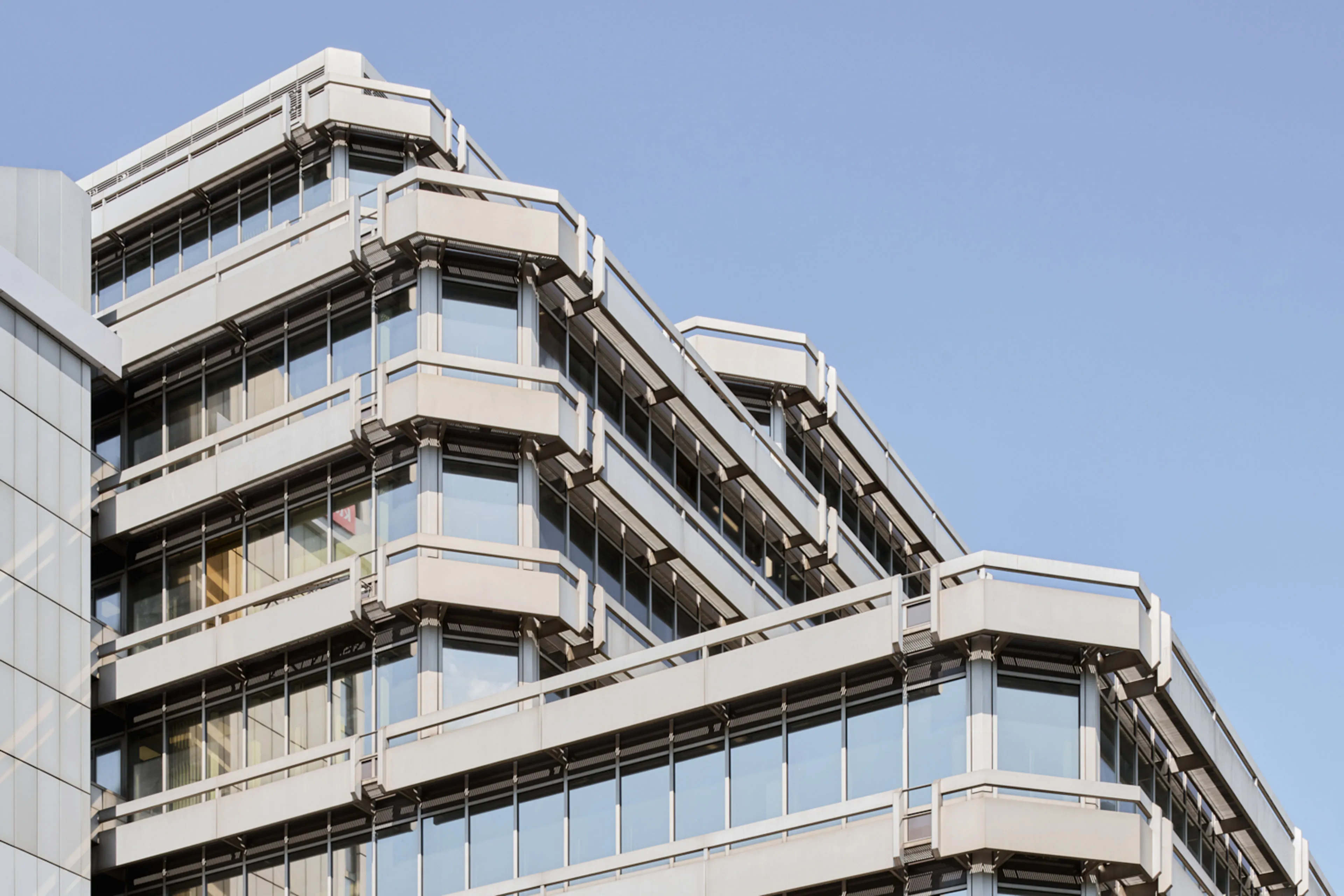 Modernes Bürogebäude mit vielen Fenstern und weißem Rahmen vor blauem Himmel.