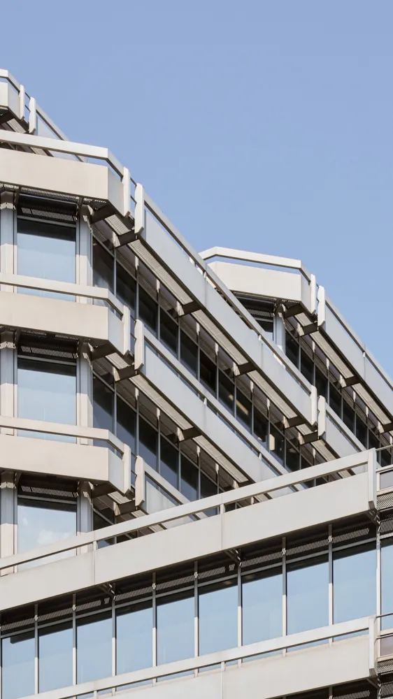 Modernes Bürogebäude mit vielen Fenstern und weißem Rahmen vor blauem Himmel.