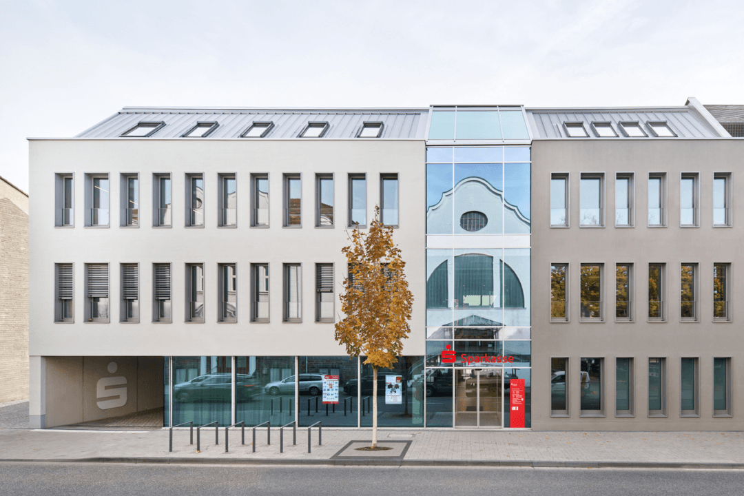 Straßenansicht eines modernen Sparkassen-Gebäudes mit klar gegliederter Fassade und mittigem gläsernen Verbinder.