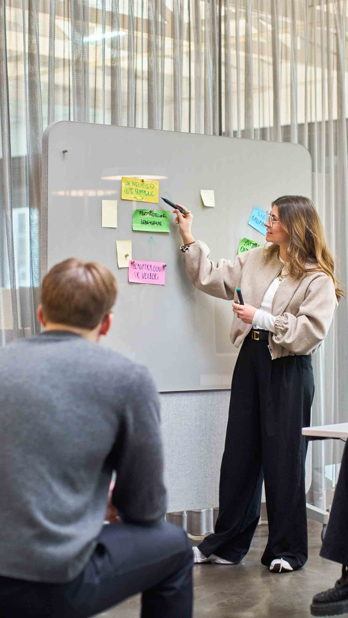 Team-Workshop im bkp-Büro: Marie Seliger am Glasboard mit Post-its, drei aufmerksame Zuhörende im lichtdurchfluteten Raum.