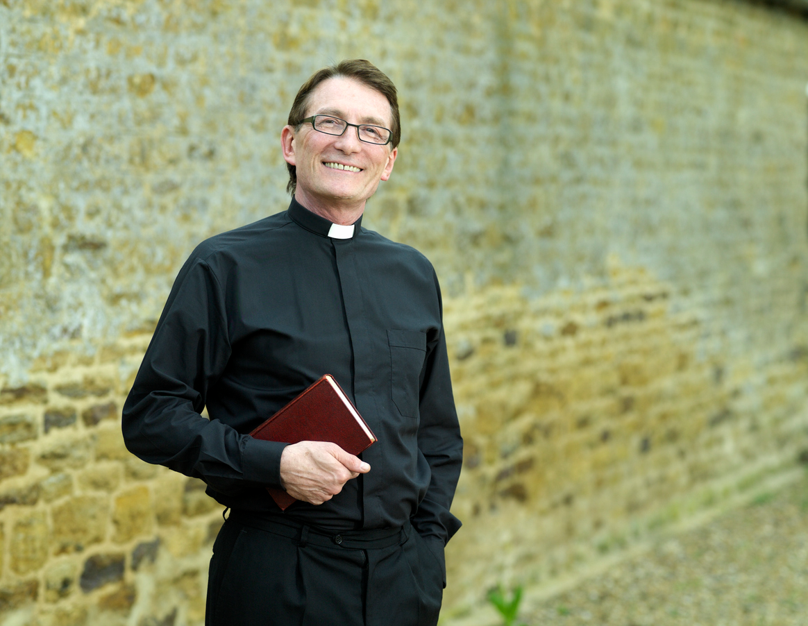 A ministry leader smiles while holding the bible under his right forearm.
