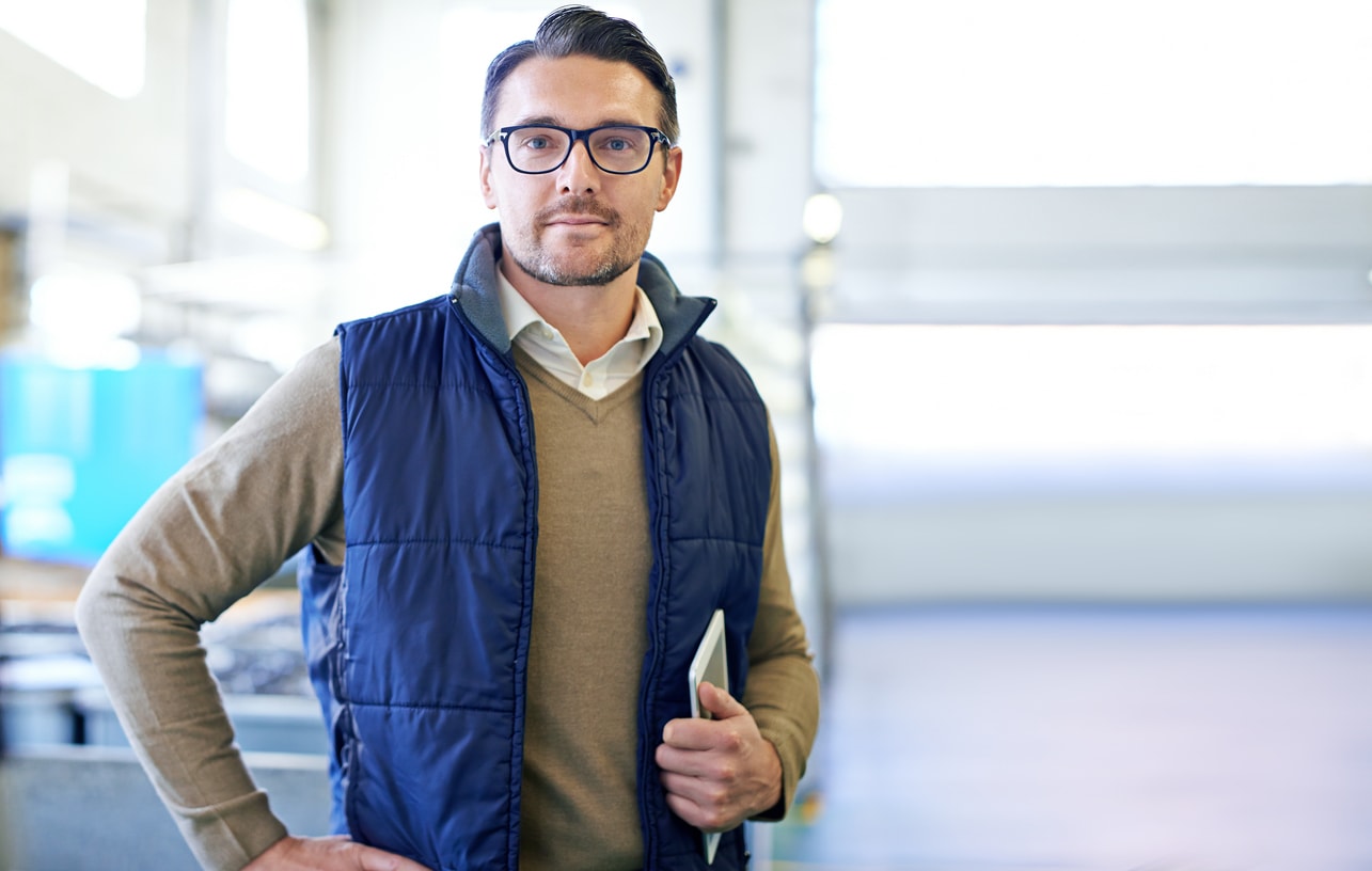 A photo of a businessman in a technical vest with glasses, holding a tablet. 