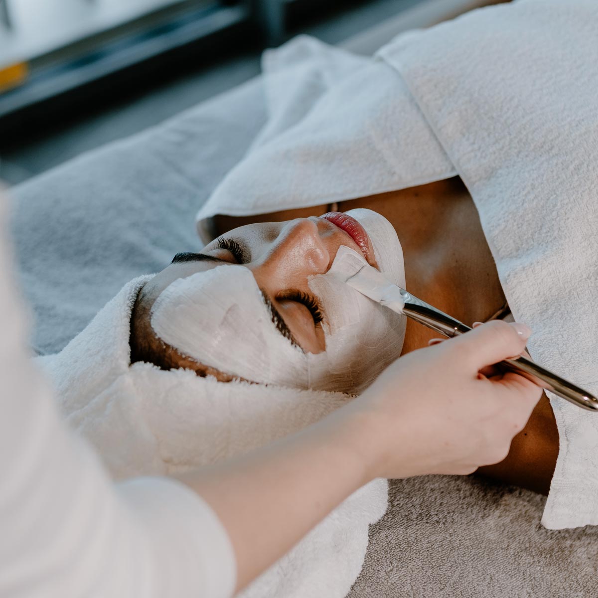 Eine Frau entspannt sich mit einer Gesichtsmaske, die von einer anderen Person mit einem Pinsel aufgetragen wird in der Salinarium Bad Dürkheim Therme