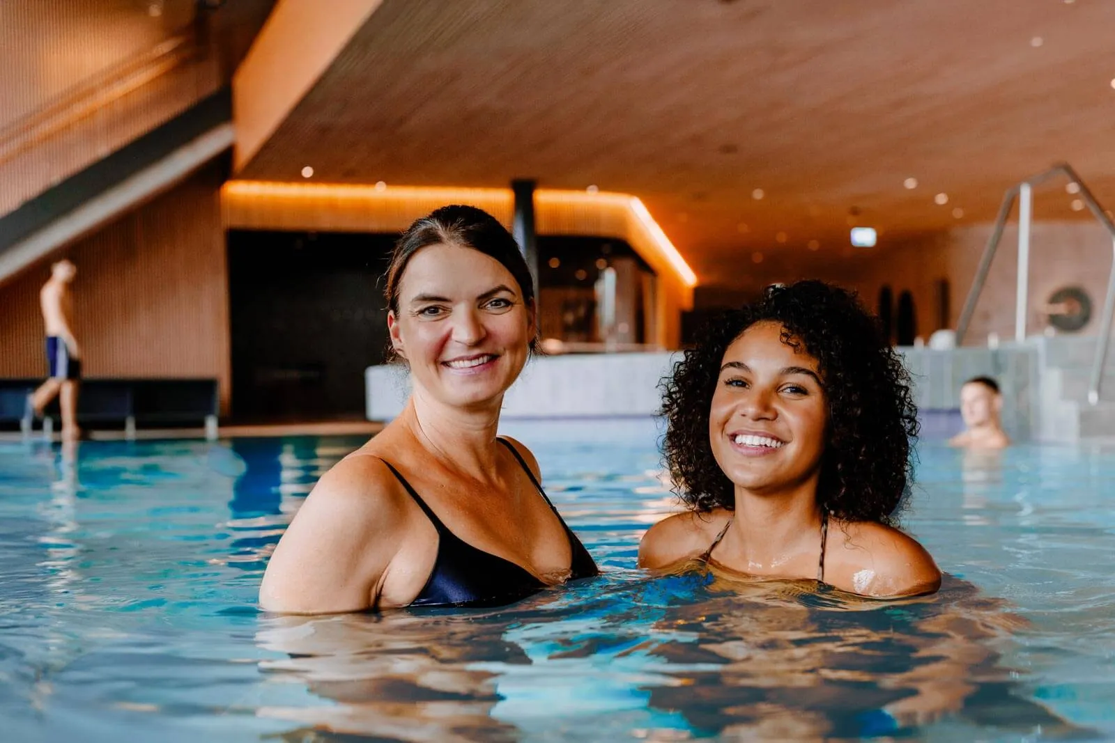 Zwei Frauen lächeln im Thermalbad der Salinarium Bad Dürkheim Therme, umgeben von warmem Holzinterieur und gedämpftem Licht.