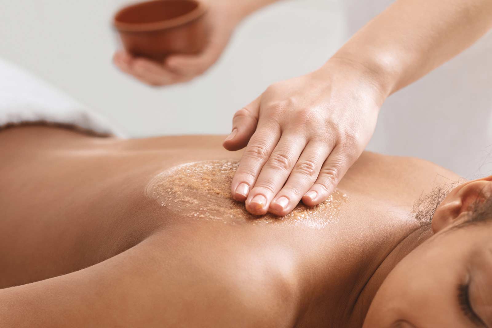 Person erhält eine Rückenpeeling-Behandlung mit einer Hand, die ein Peeling sanft auf die Haut aufträgt.