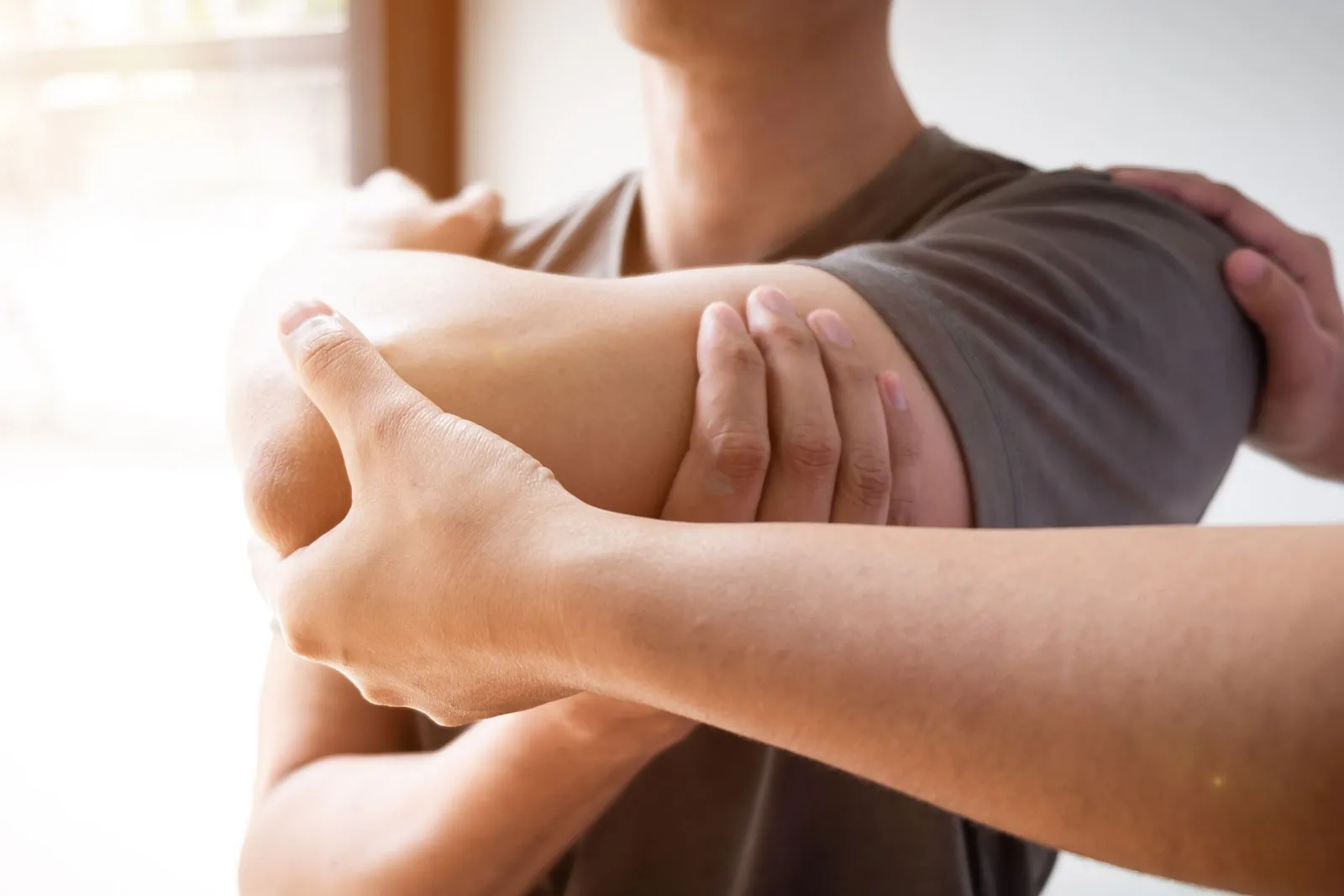 Person dehnt den Arm, indem eine andere Person ihn am Ellenbogen hält und zur Brust zieht.