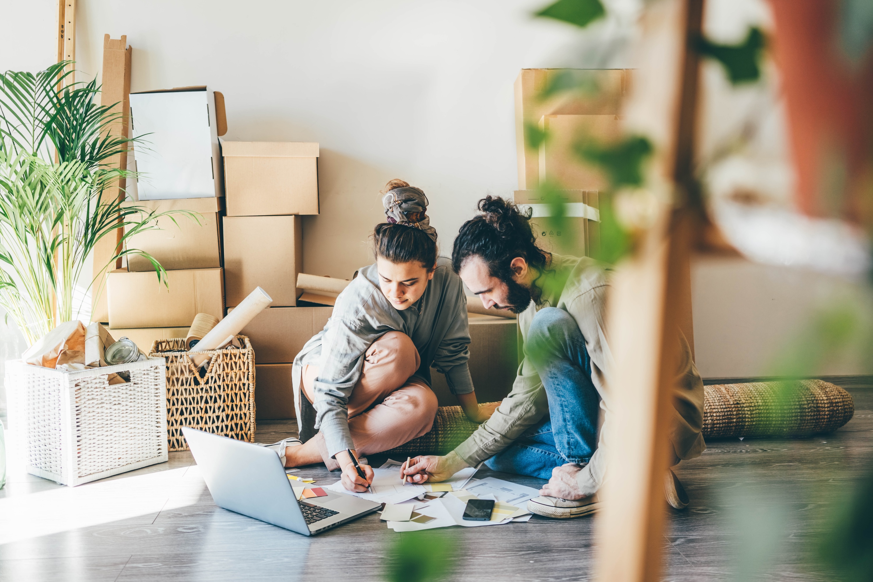 A young couple sitting on the floor of a new home, surrounded by moving boxes, planning their move-in on a laptop and paper, at Wildcat Vista in Godley, TX.