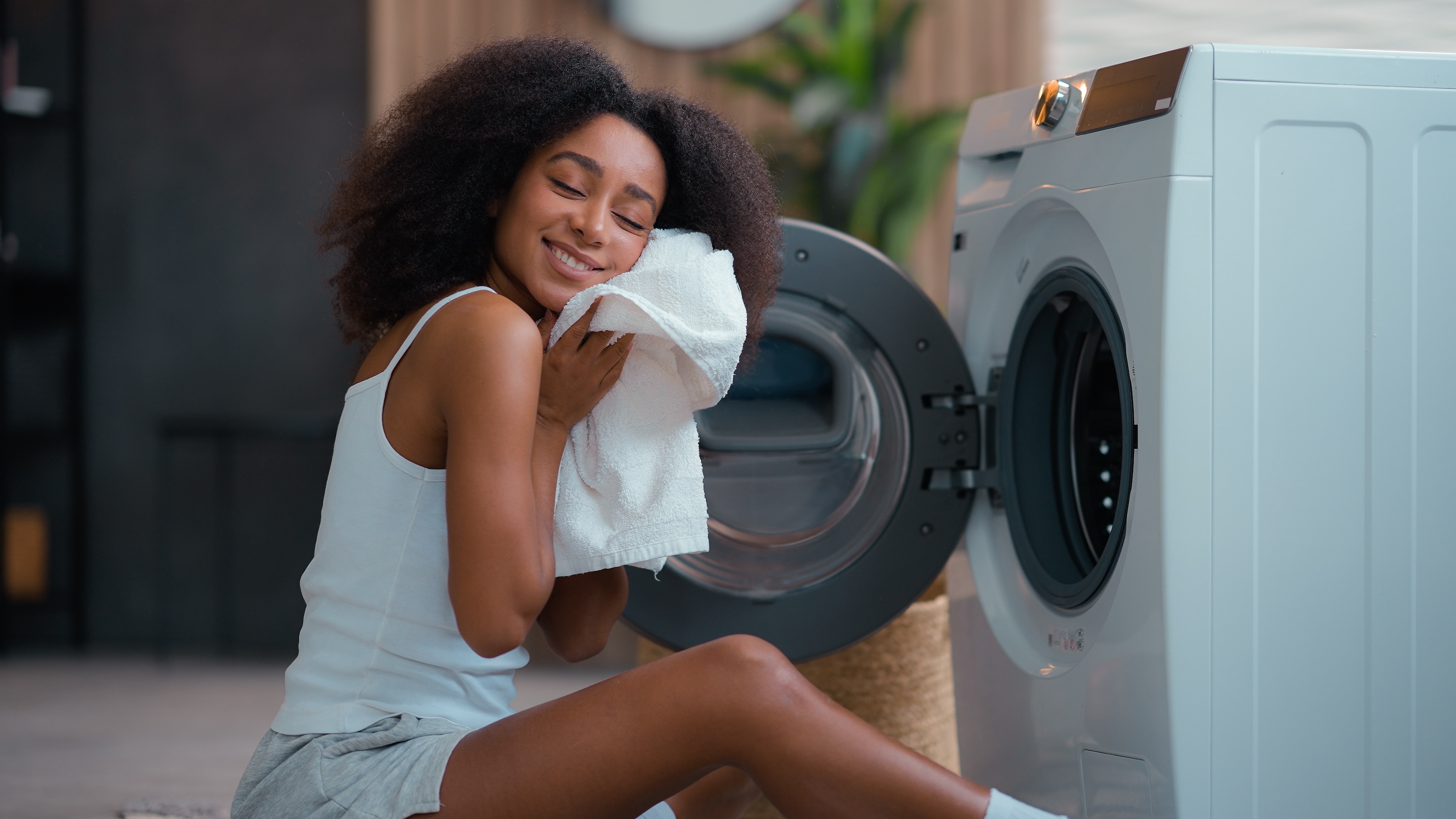 A smiling resident enjoying fresh laundry next to an in-unit washer and dryer at Wildcat Vista in Godley, highlighting the community's modern apartment features and convenient amenities.