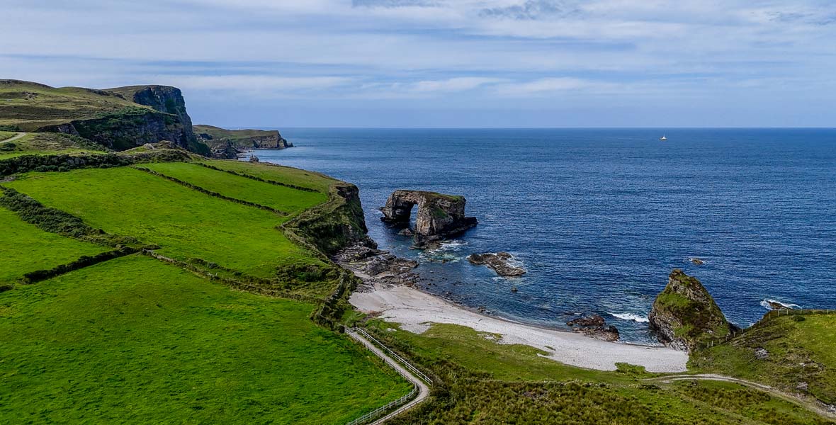 Coastal cliffs, green fields and a sea arch on the Donegal coast