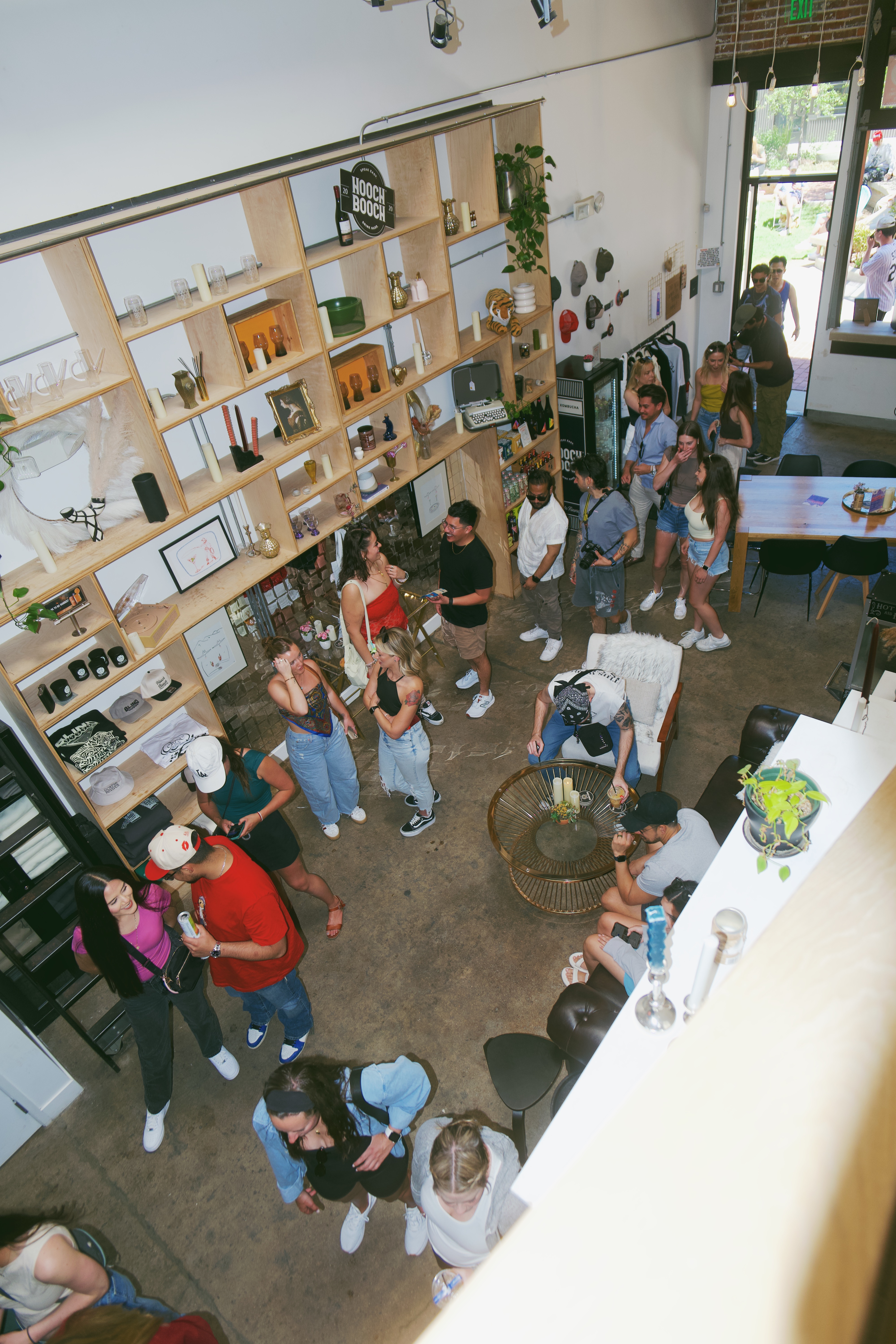 Crowded Hooch Booch retail space with wood shelving, apparel, and guests socializing