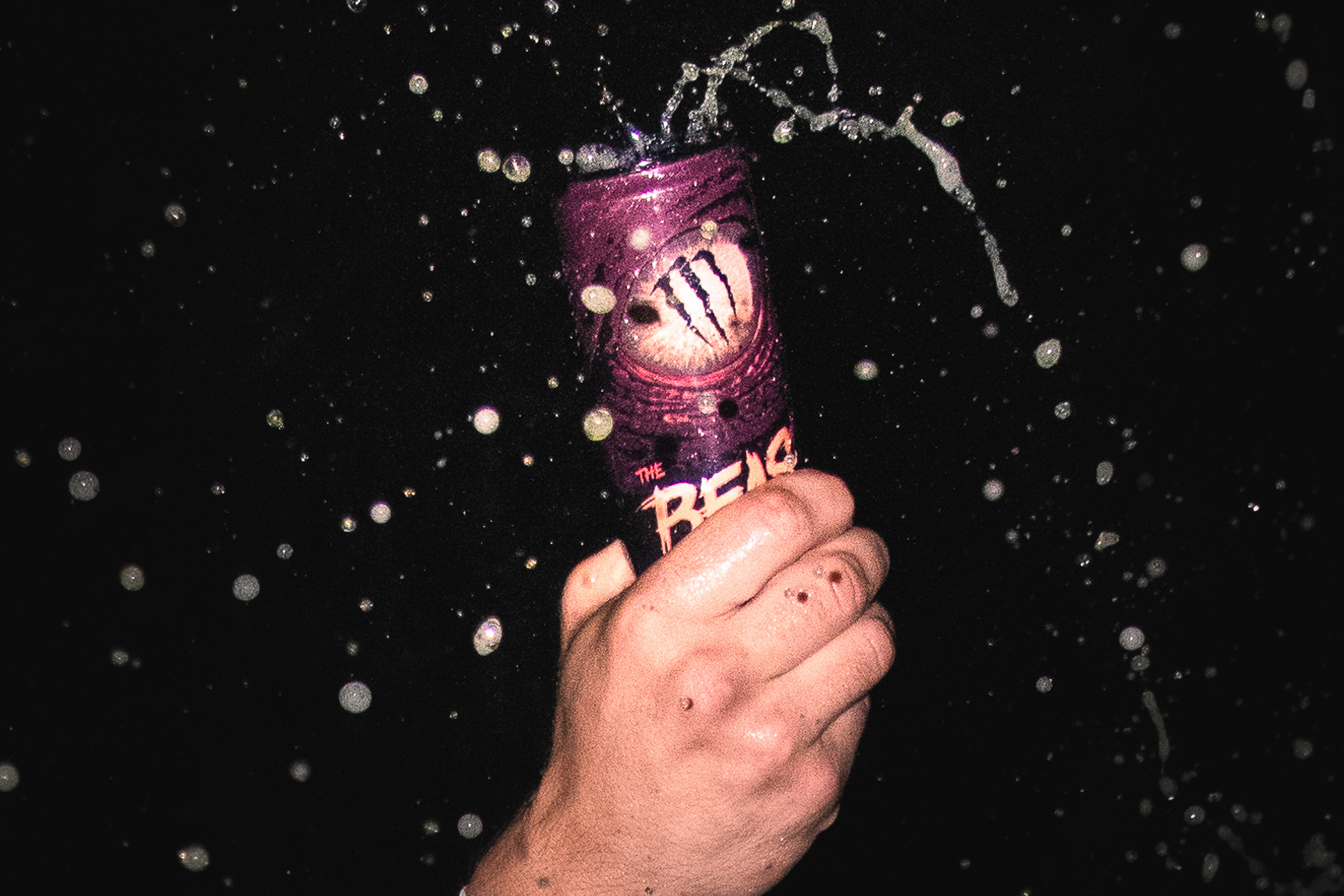 Hand gripping a Monster The Beast Unleashed can with liquid splash against black background