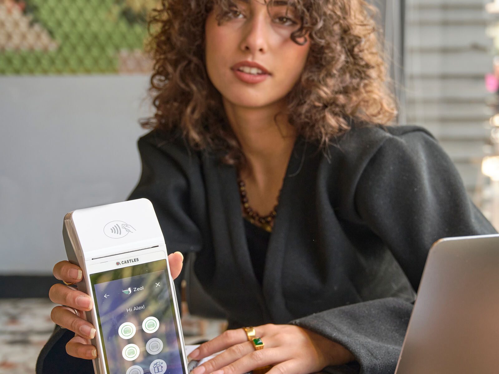 Woman curly hair desk showing payment terminal screen laptop cafe