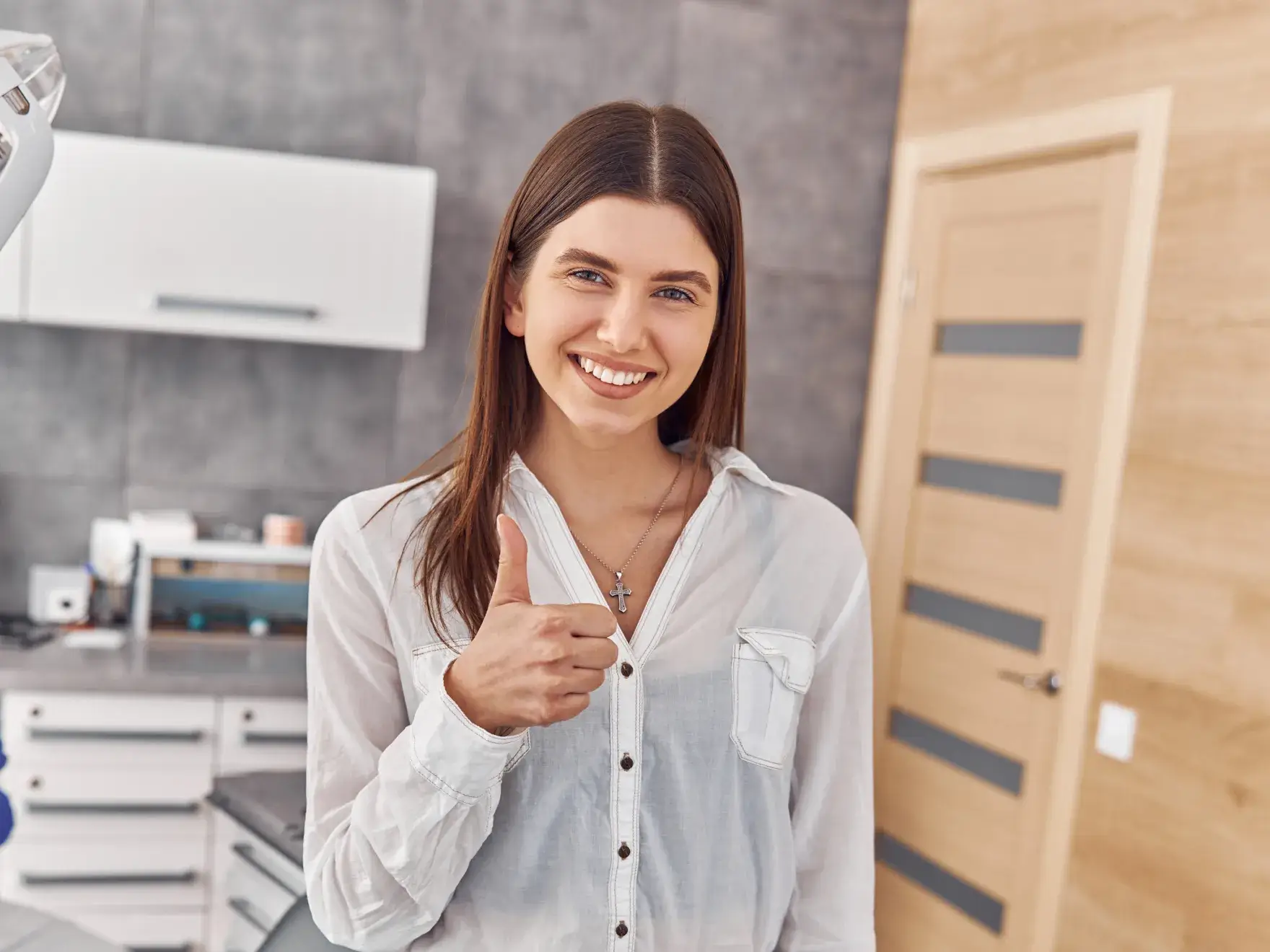 A woman smiling and giving a thumbs up in a modern indoor setting.