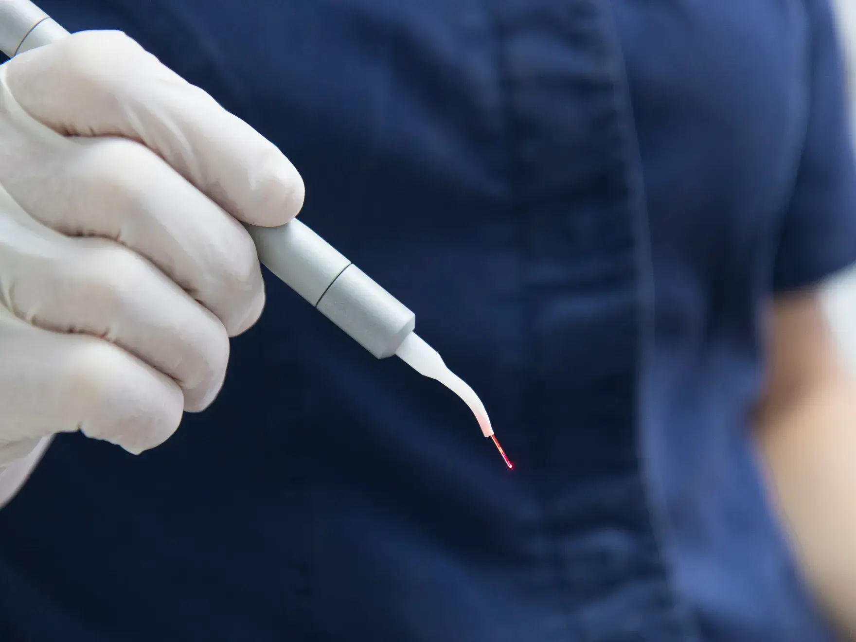 Gloved hand holding a dental tool with a red tip, against a dark shirt background.