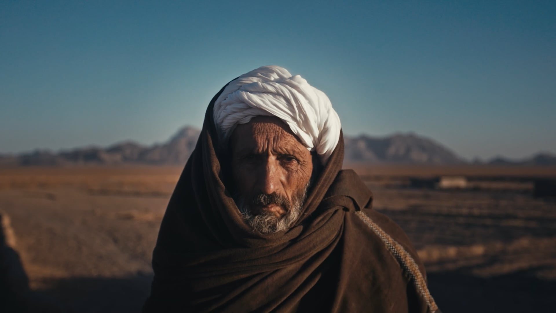 An elder in a white turban against Afghan mountains