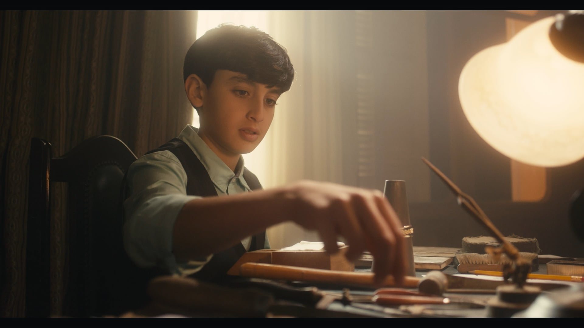 A boy at a workbench by lamplight
