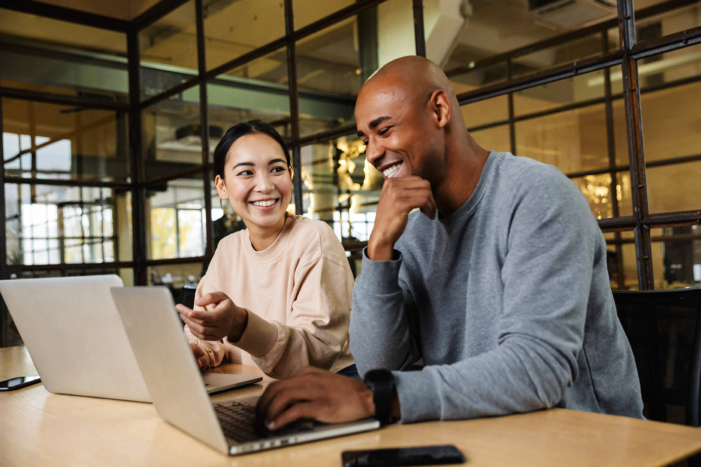 A man and a woman sitting at a table with their laptops.