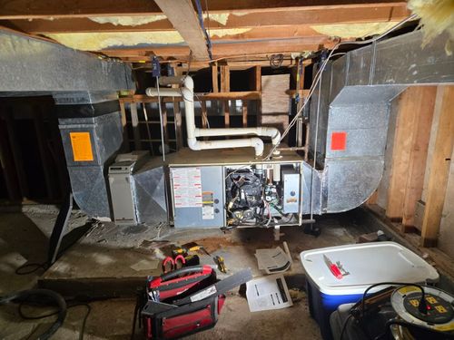 A crawlspace with a furnace and ductwork, surrounded by technician tools, indicating a repair task is underway to restore heating and ventilation efficiency.