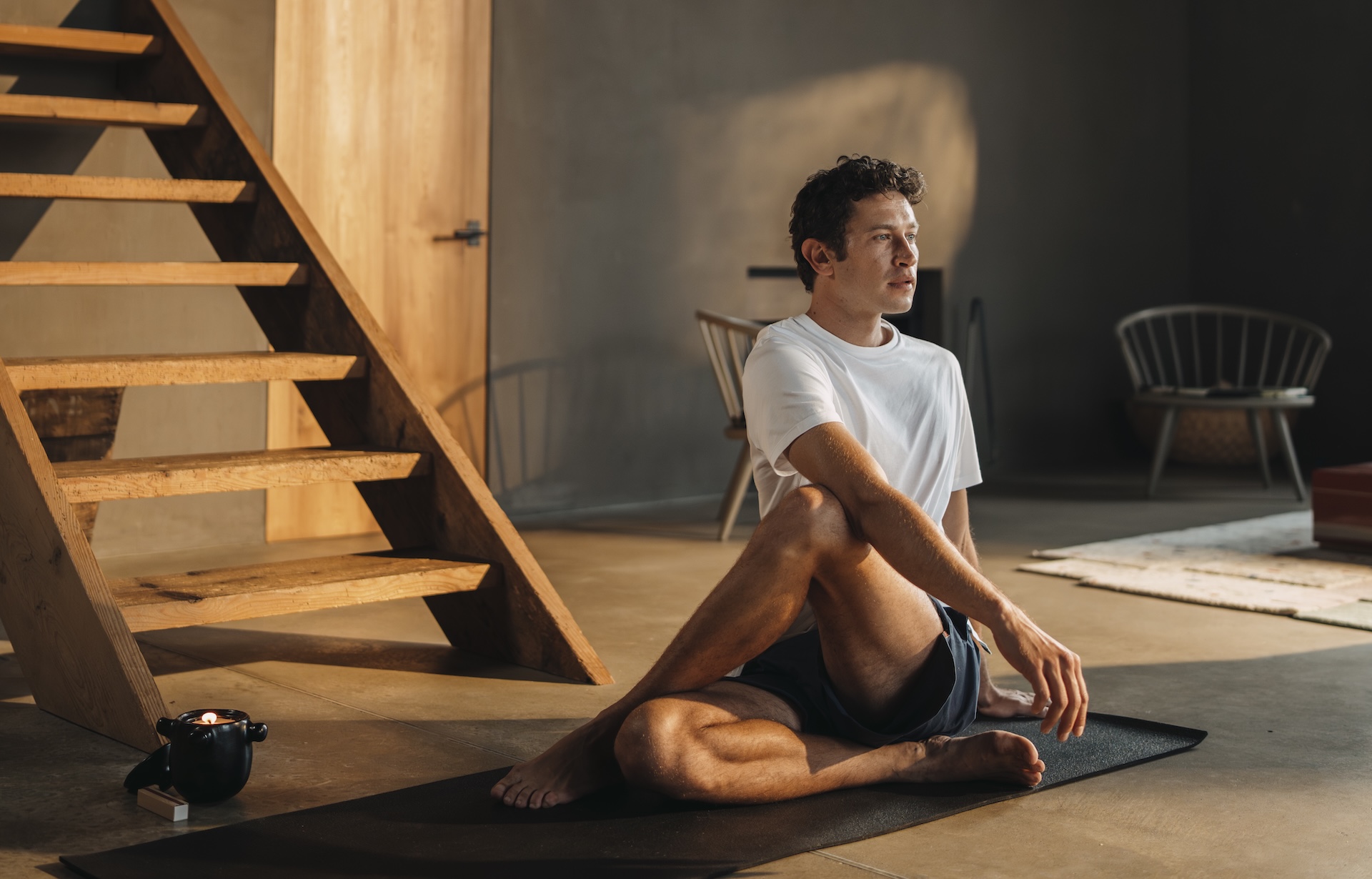 Man sitting doing yoga wearing a white Chirimoya Classic Pima cotton T-shirt and navy shorts.