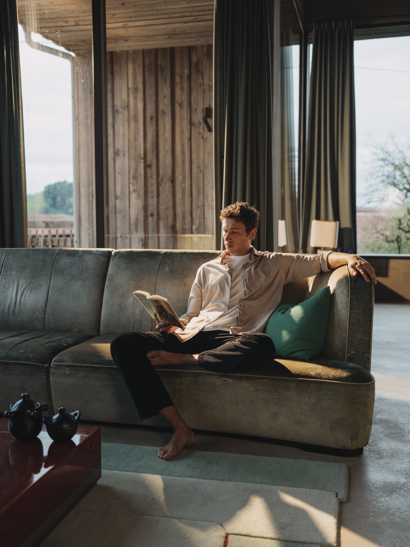 Man relaxing on a sofa reading, wearing a grey Natural Dye Chirimoya Pima cotton shirt.