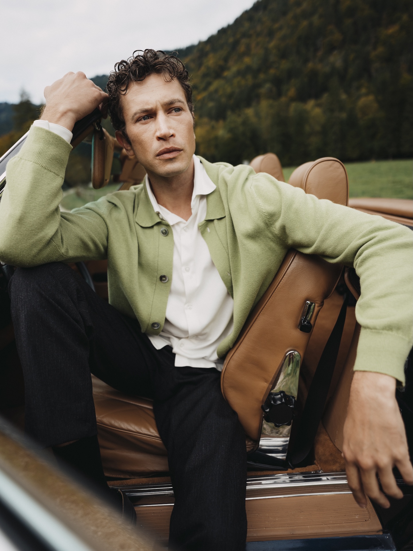 Man seated in a car wearing a light green Chirimoya Baby Pima cardigan and white shirt.