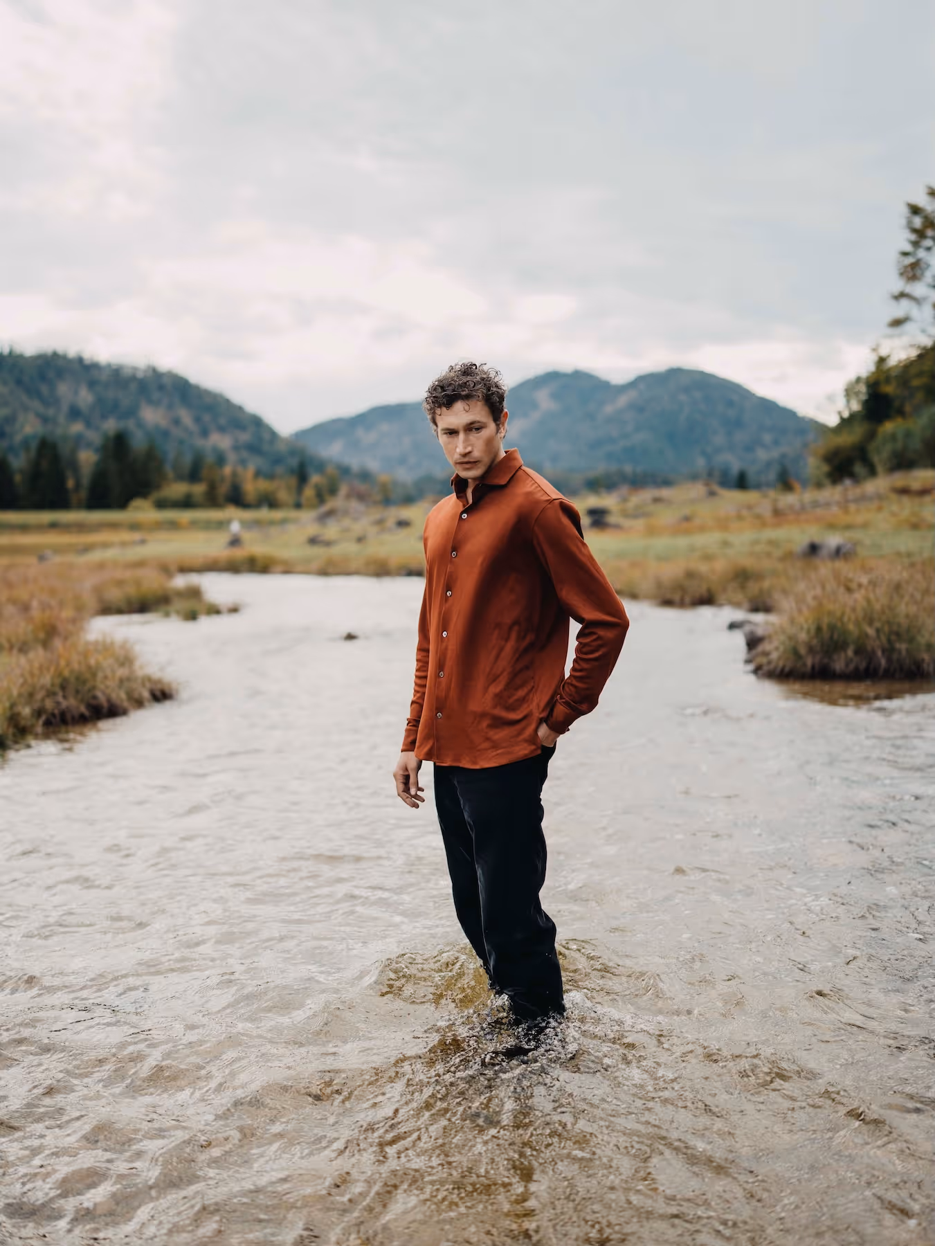Man standing in a mountain river wearing a mahogany Chirimoya Natural Dye Pima dress shirt.