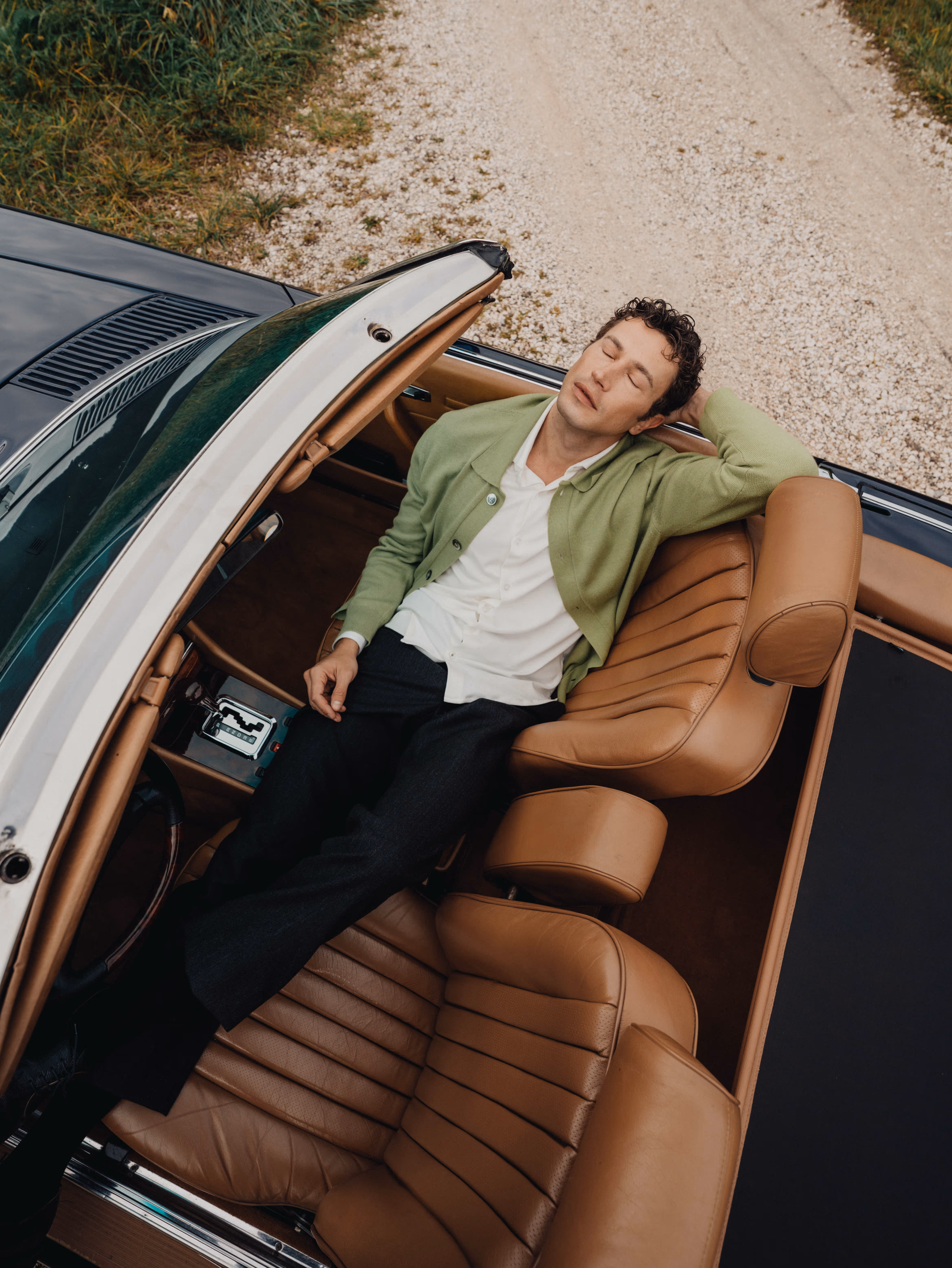Man relaxing in a vintage car, styled in a Chirimoya baby pima cardigan and white pima dress shirt.