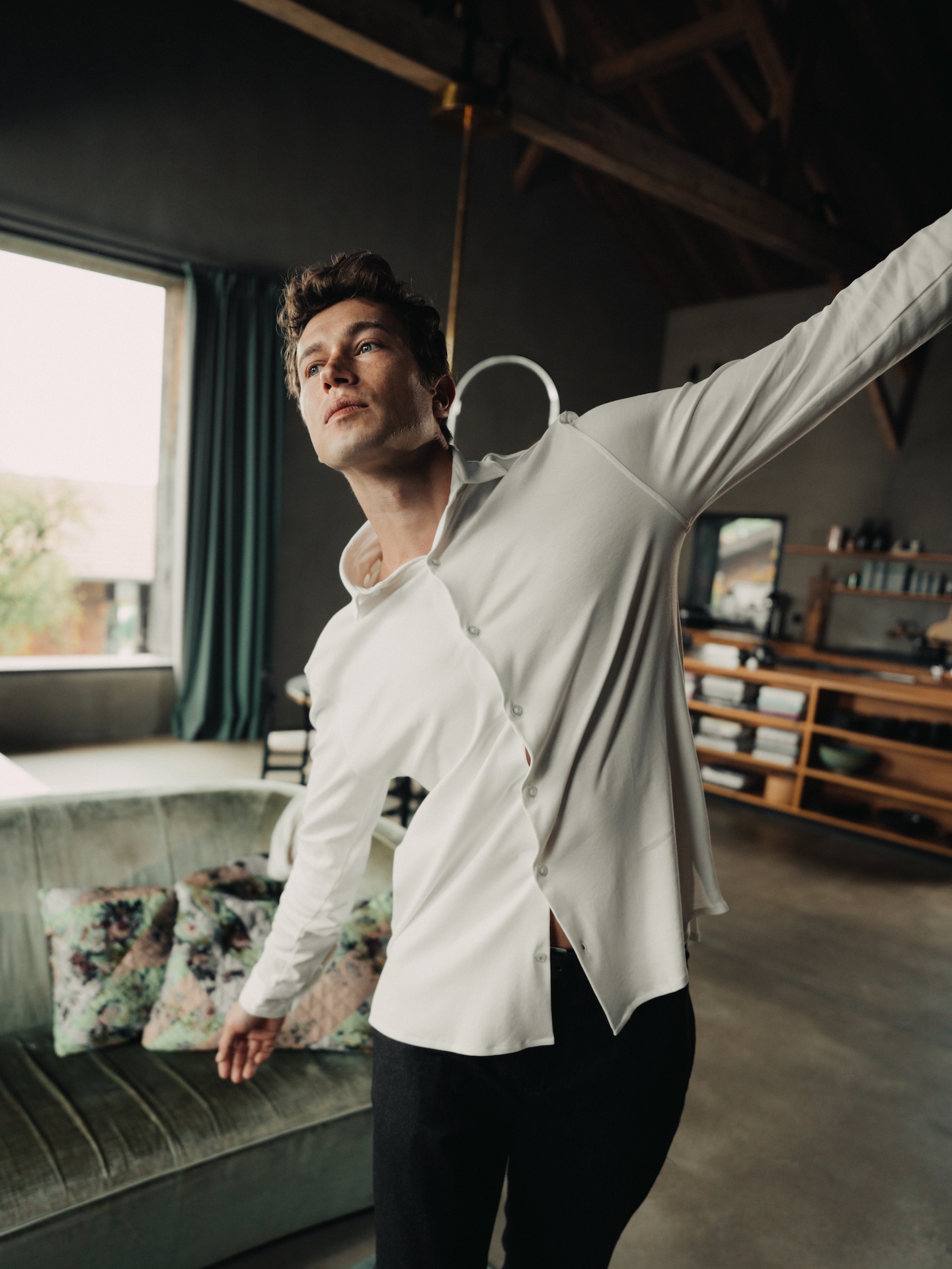 Man stretching indoors wearing a white Chirimoya Pima dress shirt in soft daylight.