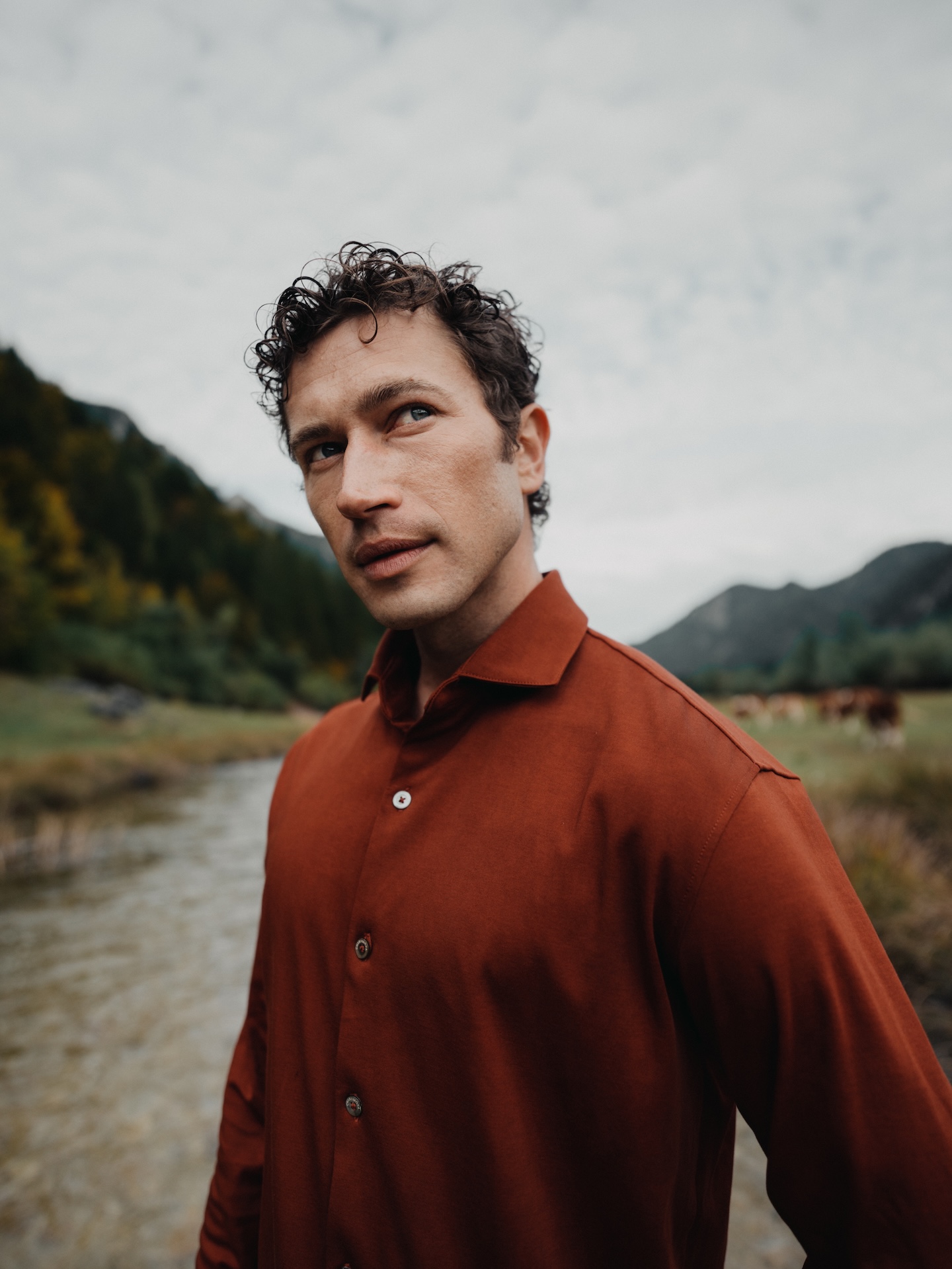 Man standing by a mountain river wearing a mahogany Chirimoya Natural Dye Pima dress shirt.