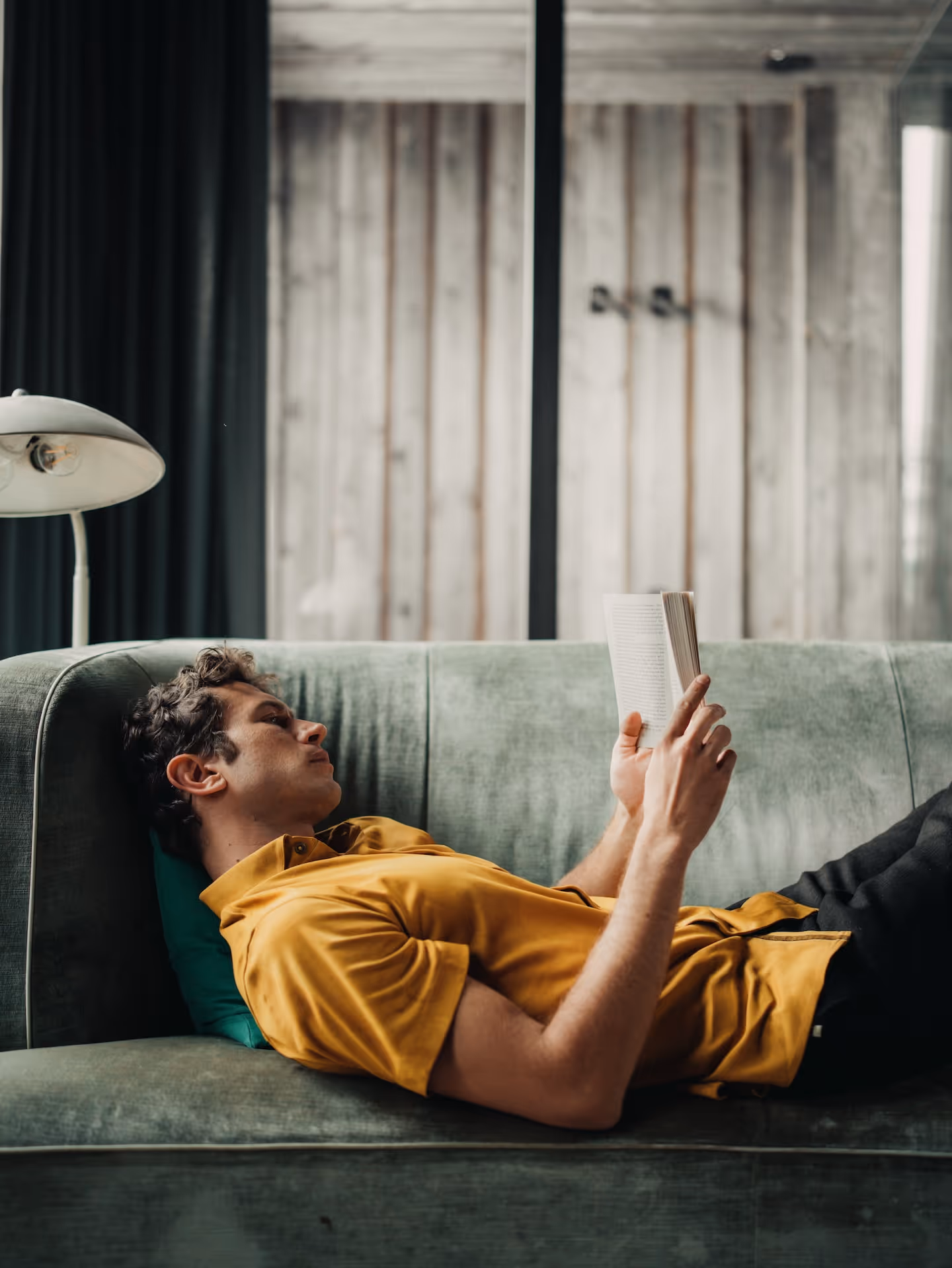 Man reading on a sofa wearing a mustard Chirimoya Natural Dye Pima t-shirt.