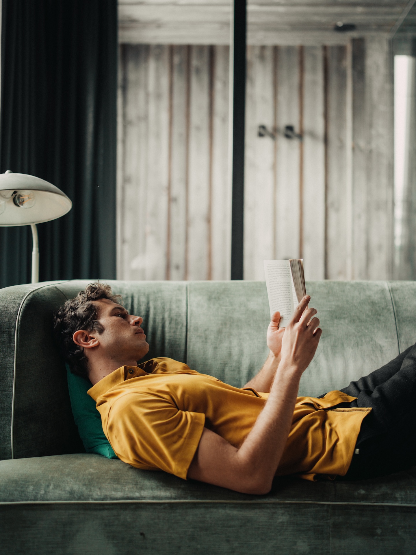 Man reading on a sofa wearing a mustard Chirimoya Natural Dye Pima t-shirt.