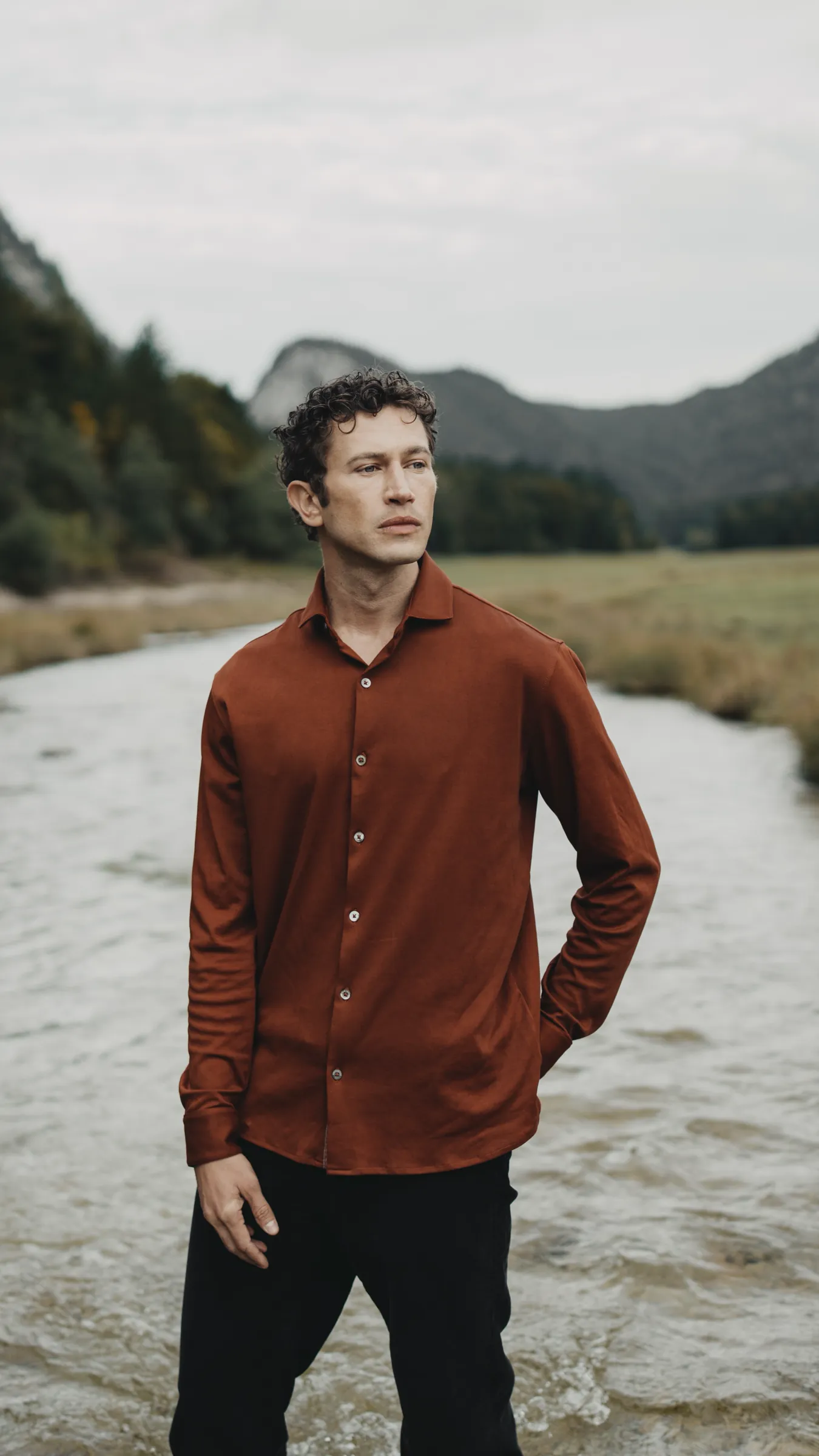 Man in a rust-coloured shirt standing in a shallow mountain stream
