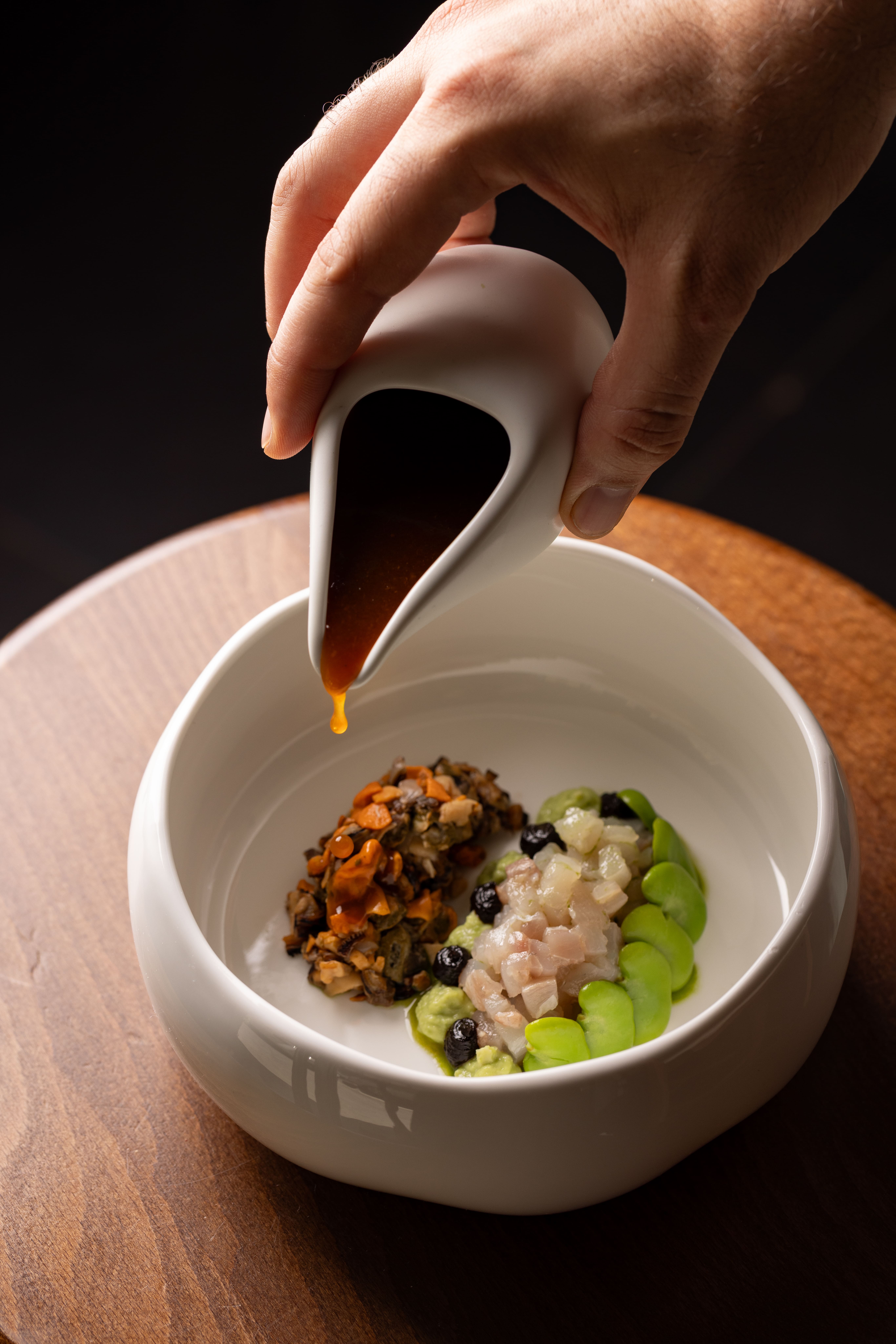 A hand sprinkling an edible pink dust on elegant green oil on a refined fine dining plate