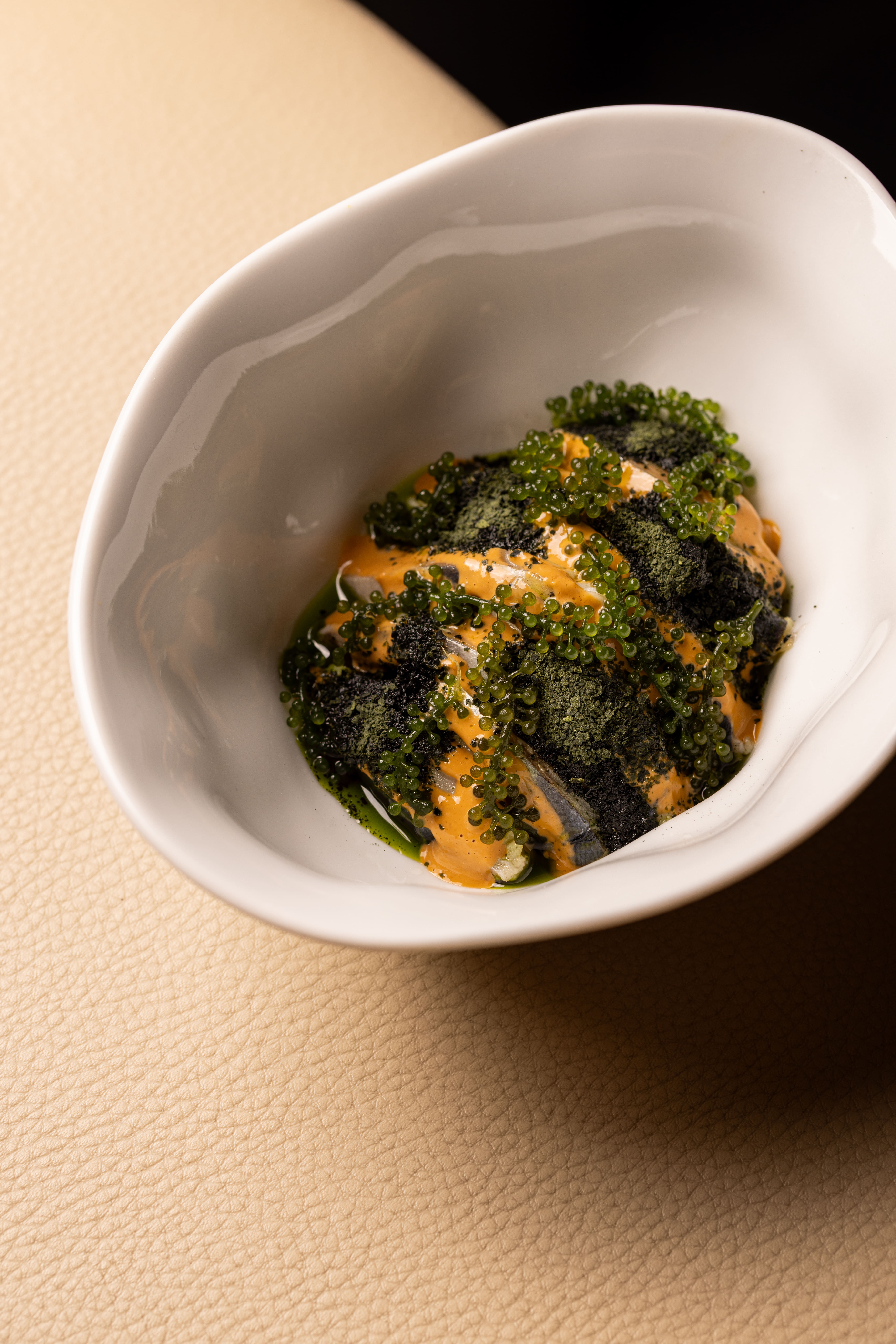 A hand sprinkling an edible pink dust on elegant green oil on a refined fine dining plate