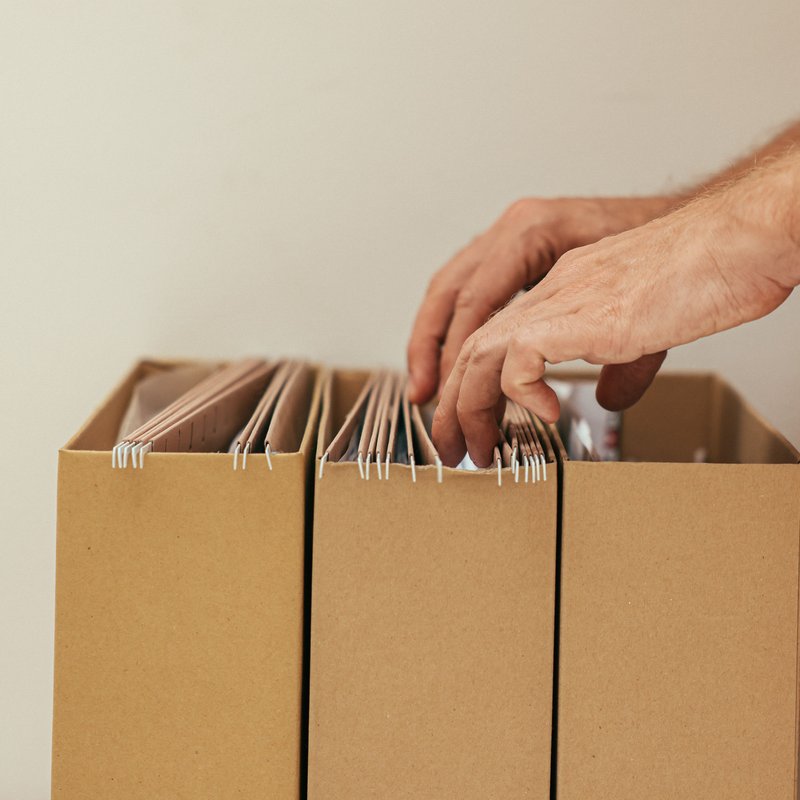 Eine Hand sucht in Hängeregistern in einer Archivbox nach Unterlagen.